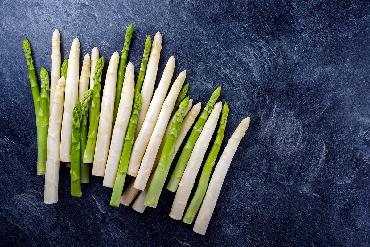 Frische weisse und grüne Spargelstangen auf dunklem Steinhintergrund.