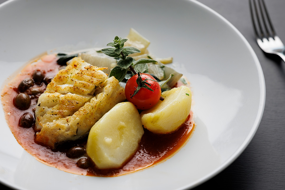 Gebratener Kabeljau auf einem weissen Teller mit Kartoffeln und rotem Jus.