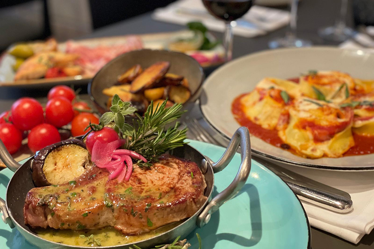 Gegrilltes Schweinskotlett in einer Pfanne mit Kräuterbutter und Gemüse im Hintergrund.